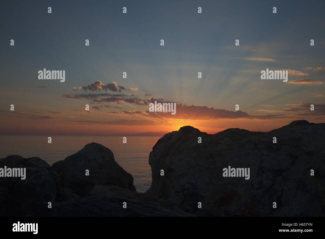 Strahlen der Sonne bei Sonnenuntergang an der Küste zwischen den Steinen In Griechenland, Kassandra. Stockfoto