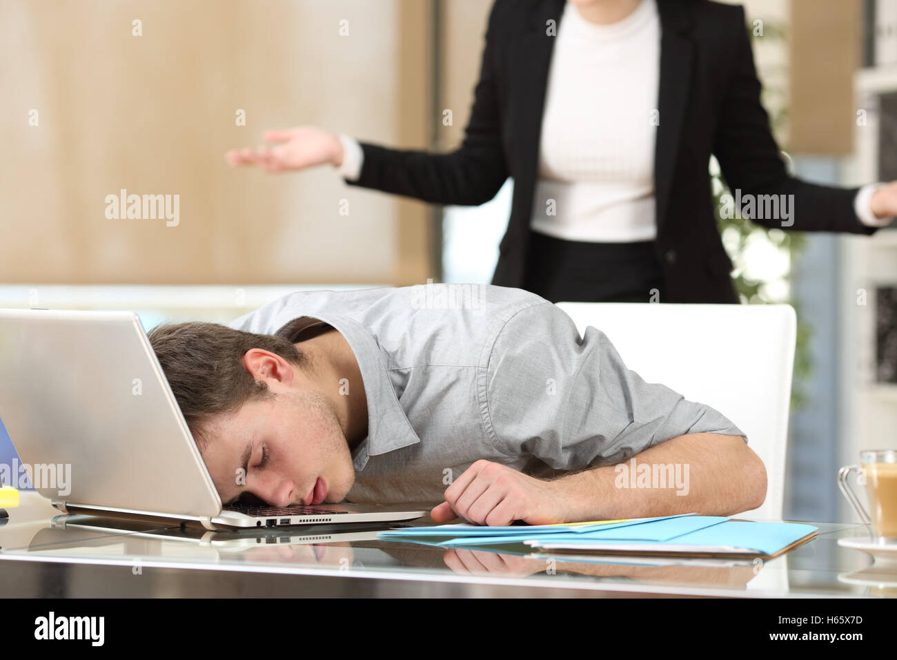 Mitarbeiter, die mit dem Gesicht über den Laptop mit seinem wütenden Chef gerade wieder im Büro schlafen Stockfoto