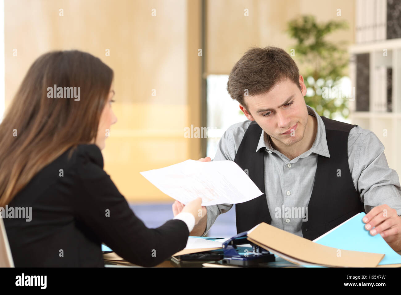 Inkompetente Geschäftsmann mit ungeordneten Desktop Teilnahme an einen verärgert Client, indem er ihr einen schmutzigen Bericht im Büro Stockfoto