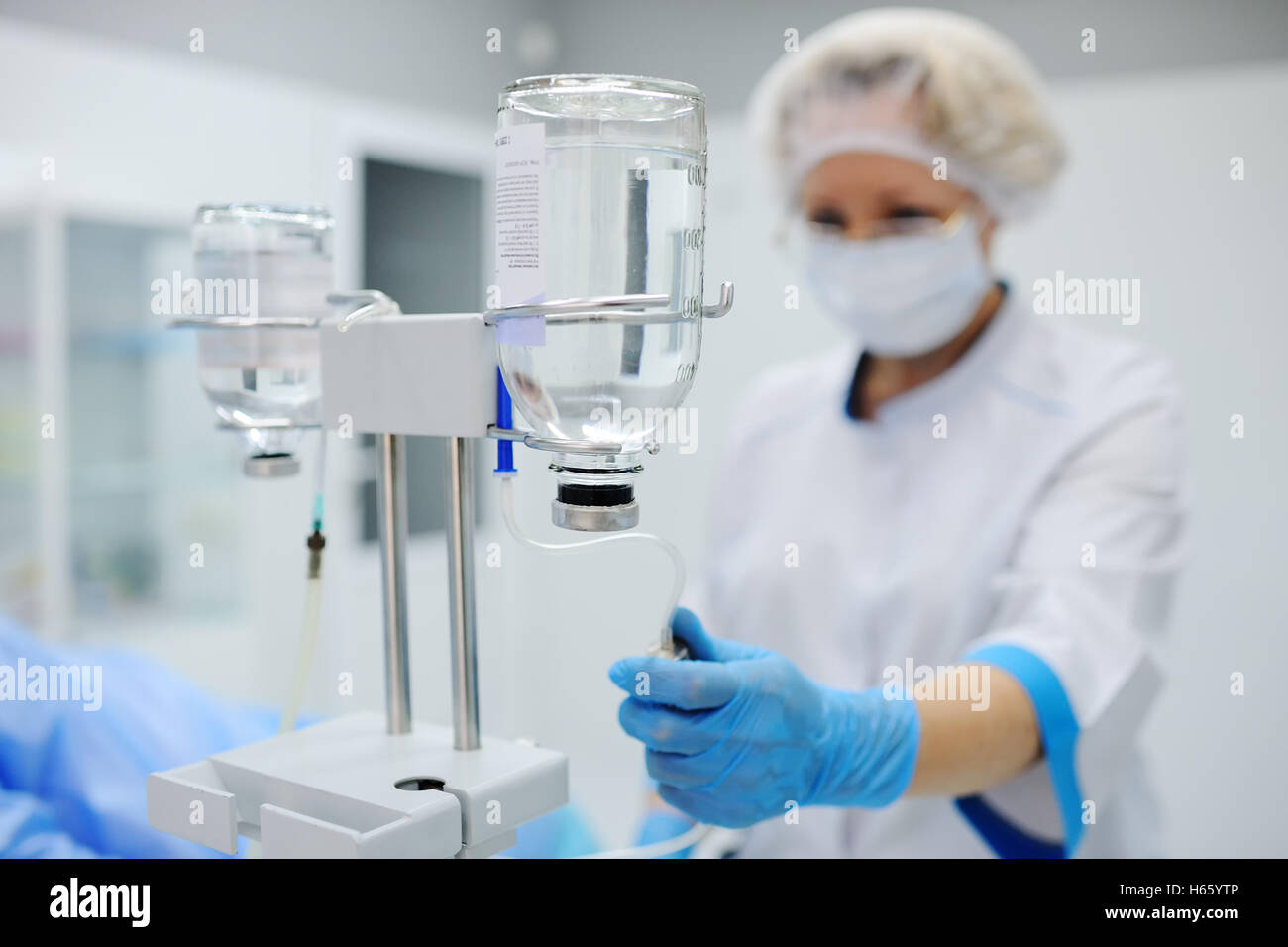 Arzt Frau in medizinischen Maske und sterile Handschuhe, die ein Patient für die Operation vorbereiten. Pipette in eine Vene Nahaufnahme auf einem Hintergrund von Stockfoto