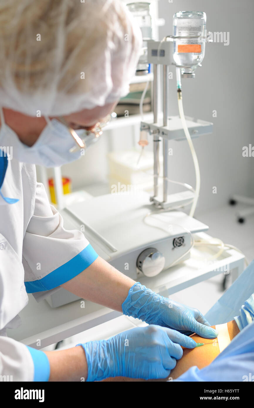Arzt Frau in medizinischen Maske und sterile Handschuhe, die ein Patient für die Operation vorbereiten. Pipette in eine Vene Nahaufnahme auf einem Hintergrund von Stockfoto