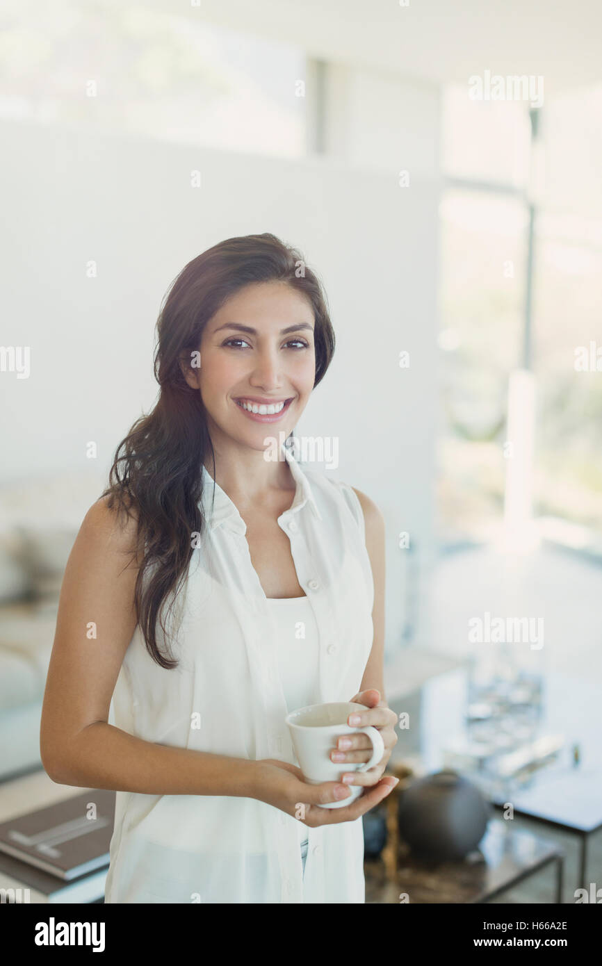 Porträt lächelnde Brünette Frau trinken Kaffee im Wohnzimmer Stockfoto