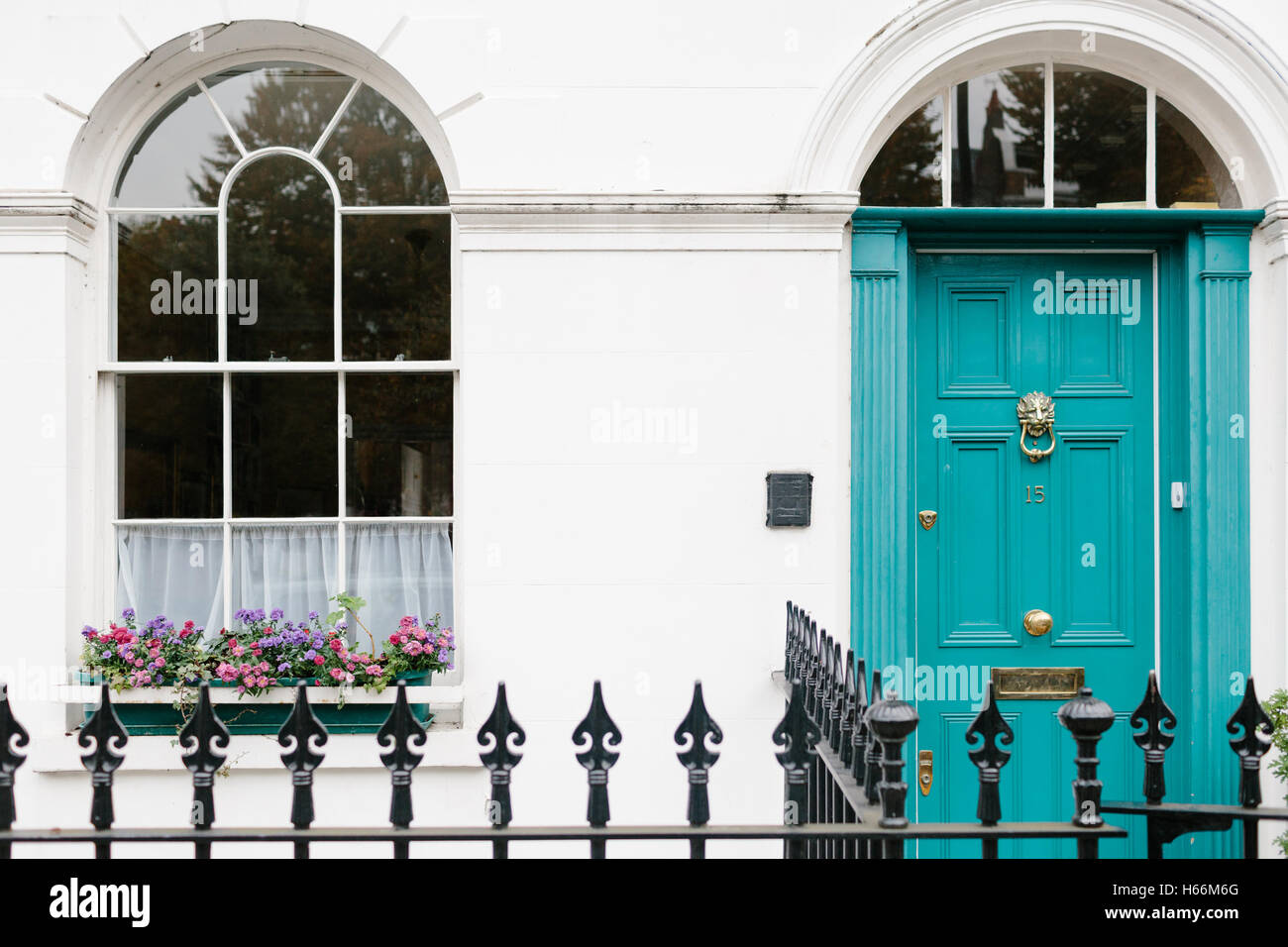 Aqua-farbige Haustür und gewölbtes Fenster mit bunten Blumen auf einer Londoner Straße, komplett mit schwarzen Zaun. Stockfoto
