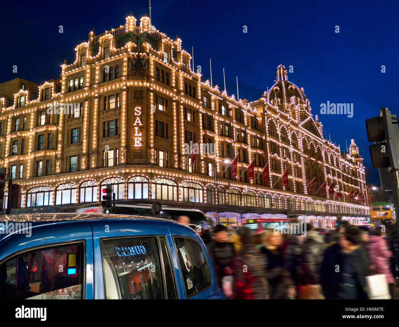 Kaufhaus Harrods im Winter mit Einkäufern verwischen nachts die geschäftige Gegend von ULEZ mit dem Season Sale-Schild Käufer und vorbeifahrende Taxis Knightsbridge London SW1 Stockfoto