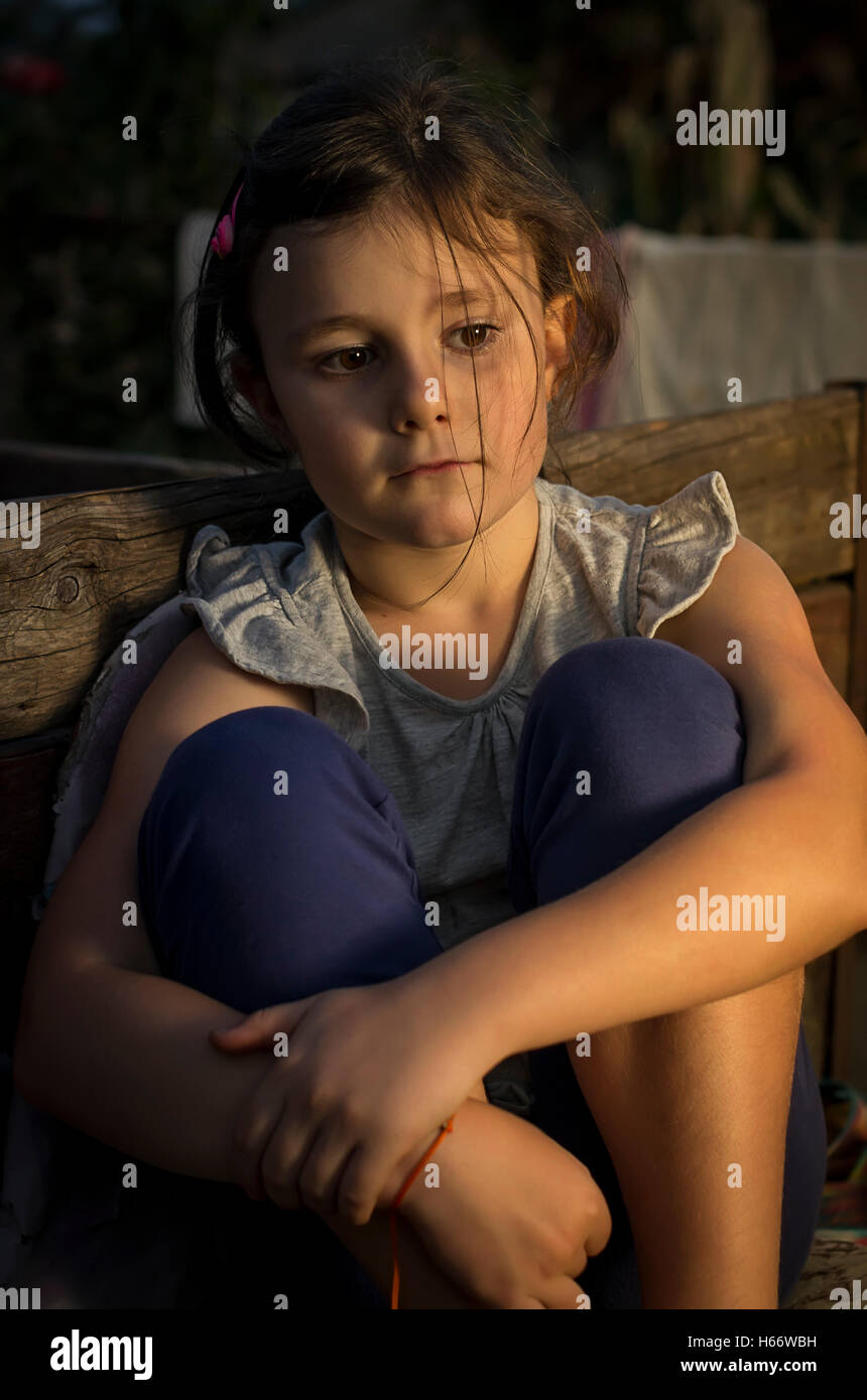 Sieben Jahre altes Mädchen in Landschaft in ein Abendlicht traurig auf einem Stuhl sitzen. Stockfoto