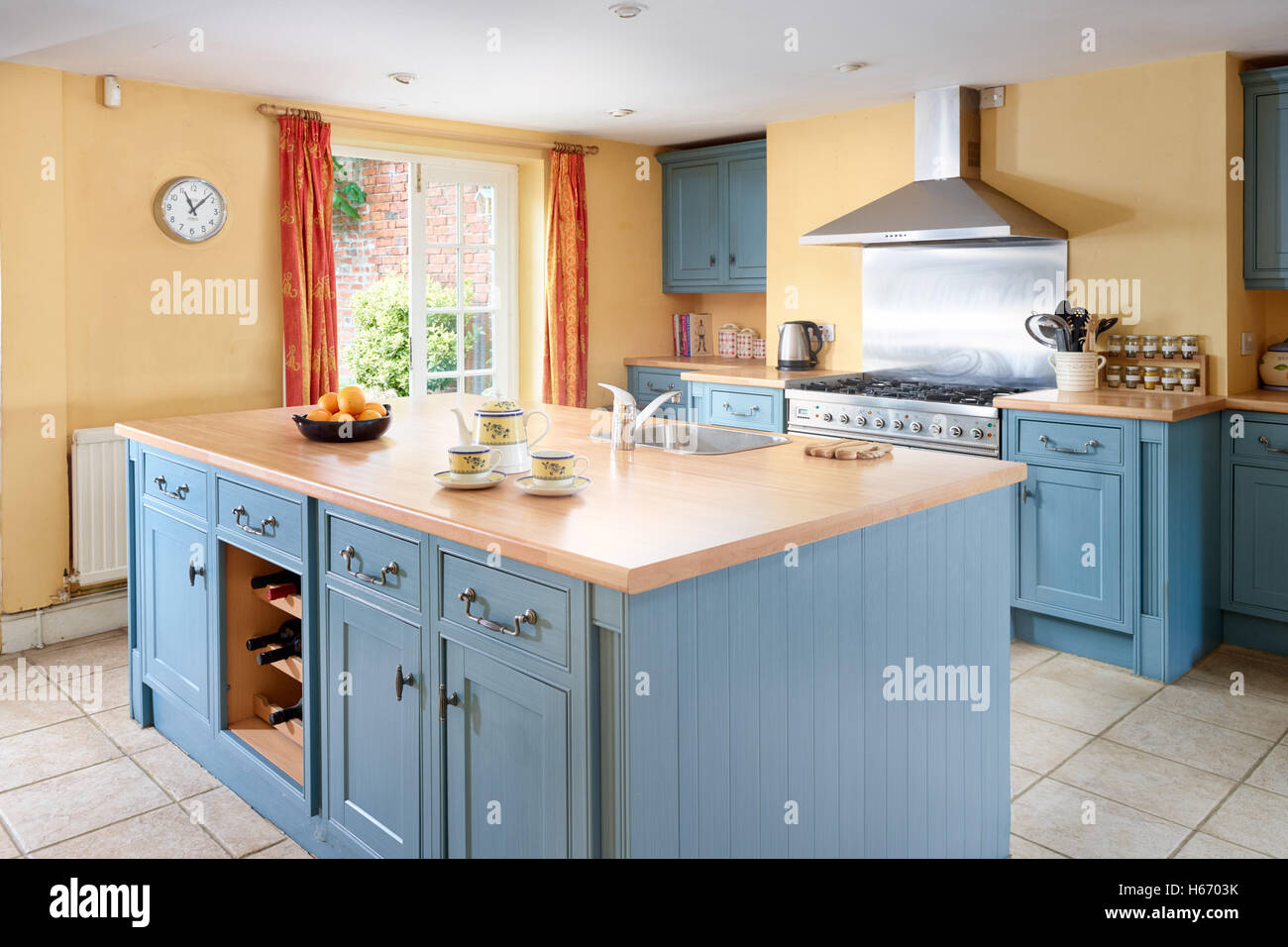 Eine große Landhausküche mit traditionell gestalteten Einheiten in blau mit massivem Holz Arbeitsflächen, gelbe Wände & ein Küchenherd Stockfoto