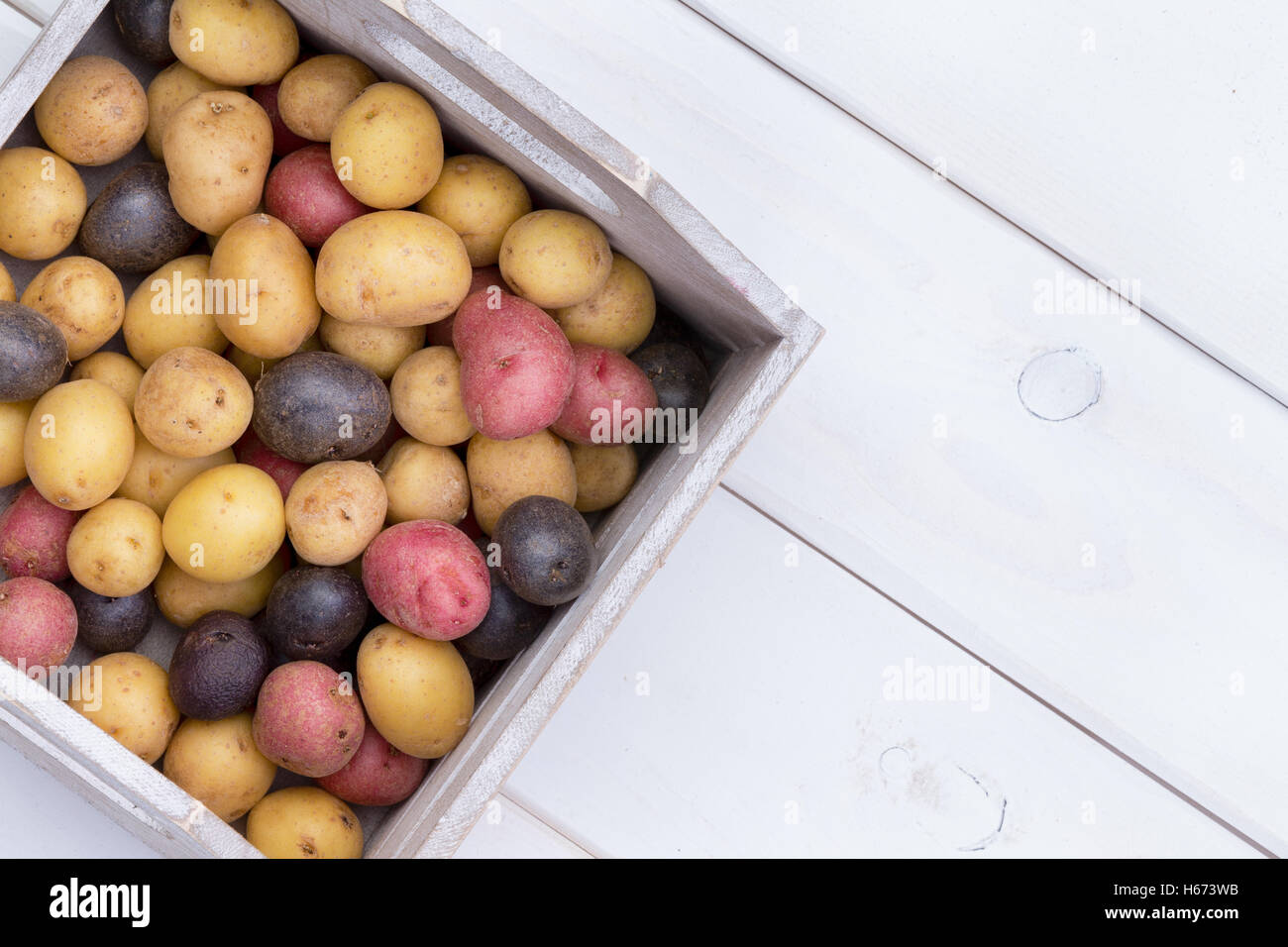 Holzkiste gefüllt mit bunten frischen rohen Babykartoffeln am Bauernmarkt auf einem weißen Holztisch von oben gesehen Stockfoto