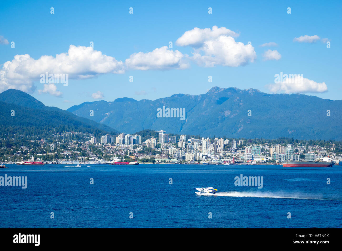 Ein Wasserflugzeug bekommt bereit zum Abheben im Hafen von Vancouver.  North Vancouver, Britisch-Kolumbien, Kanada ist in der Ferne. Stockfoto