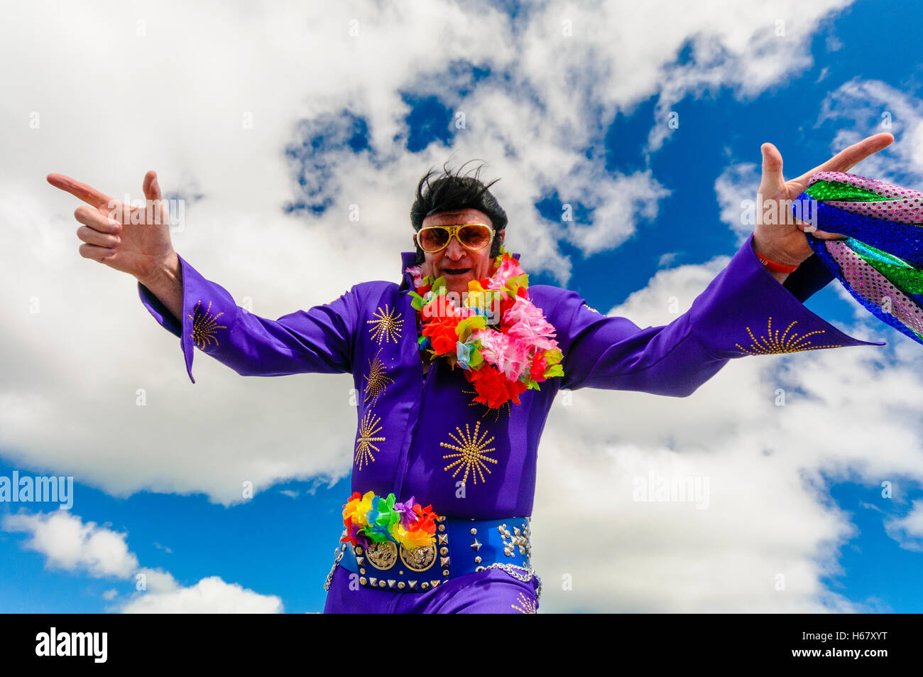 Elvis-Imitator trägt einen lila Overall, Sonnenbrille und ein Kranz von Blumen Stockfoto