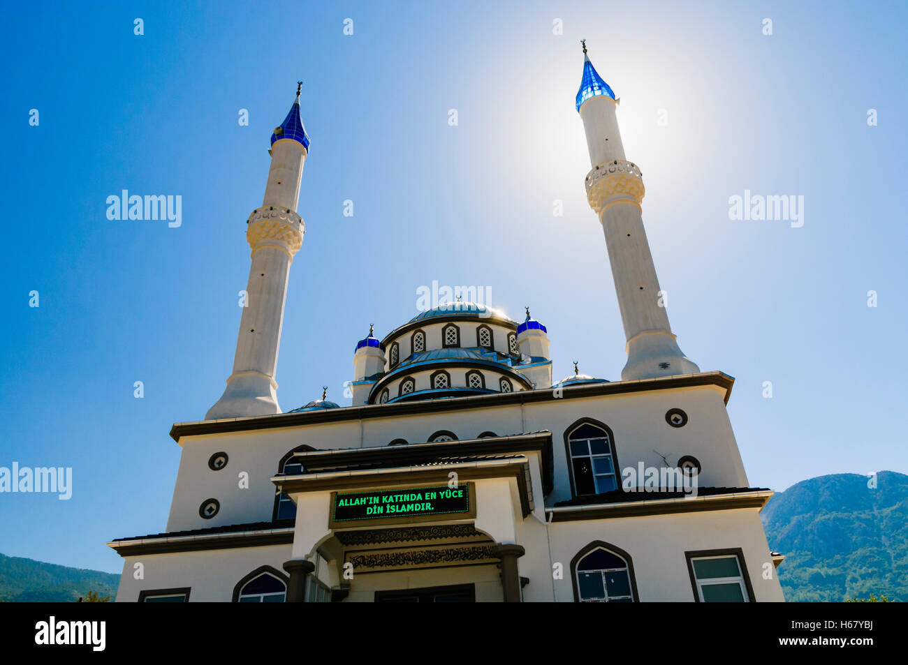 Sonne hinter dem Minarett einer Moschee mit einer Botschaft auf Türkisch: „Die höchste Religion in Allah ist der Islam“. Stockfoto