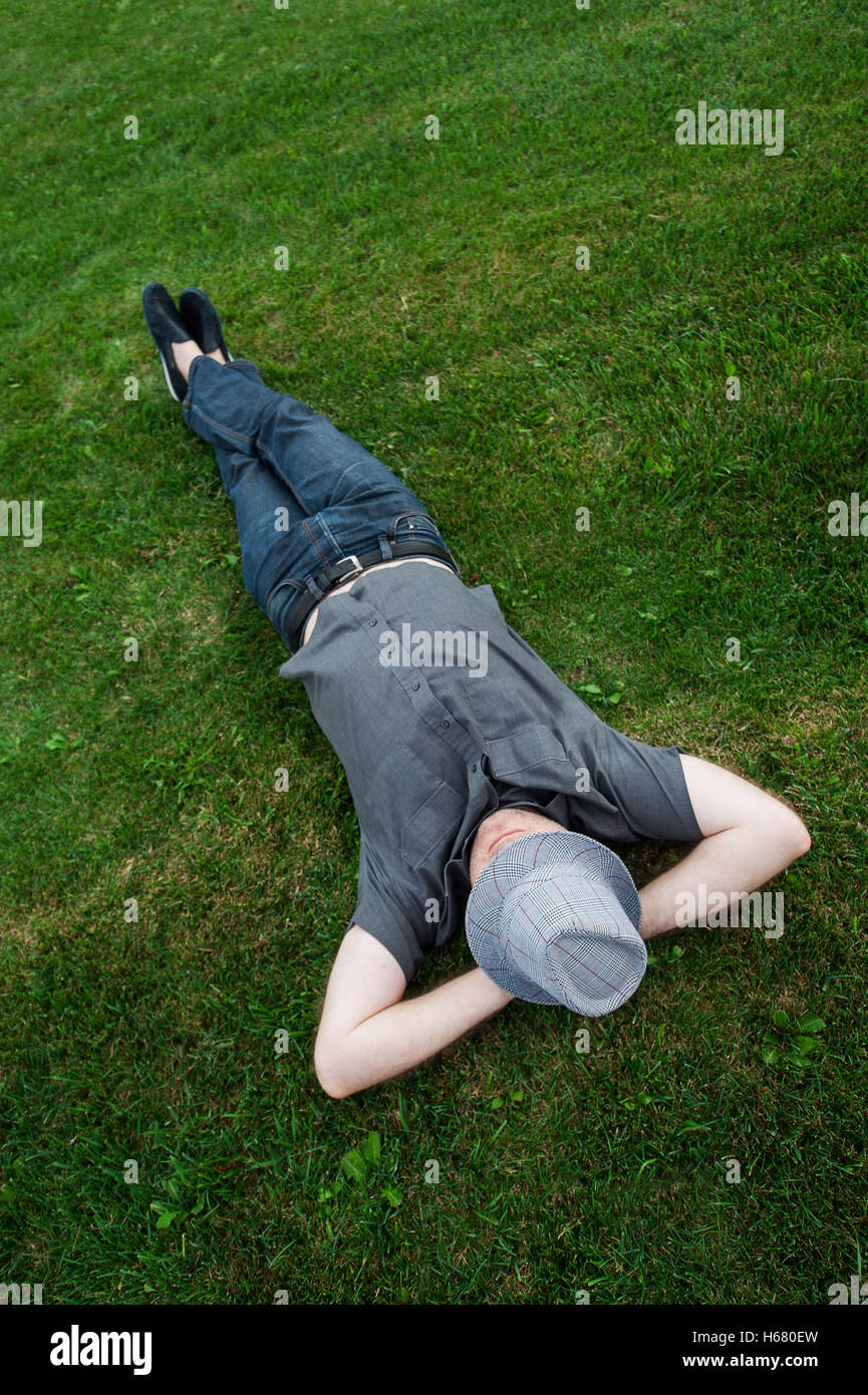 Geschäftsmann, liegend in einem Feld auf dem grünen Rasen mit dem Hut über sein Gesicht. Passives Einkommen Stockfoto