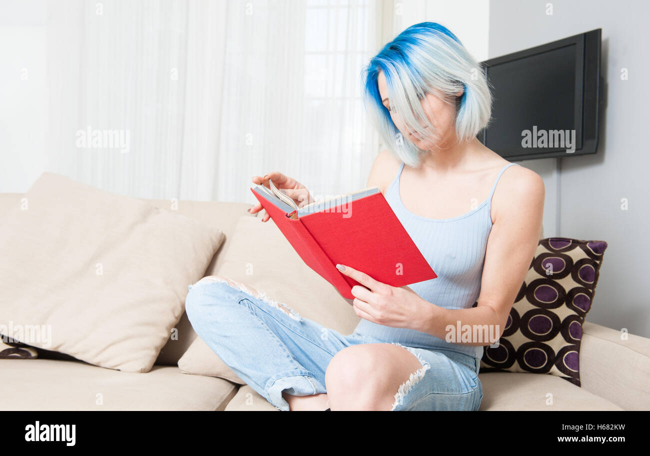 Junge hübsche Teen Frau auf Sofa sitzen und rotem Einband Buch zu Hause im Wohnzimmer Stockfoto