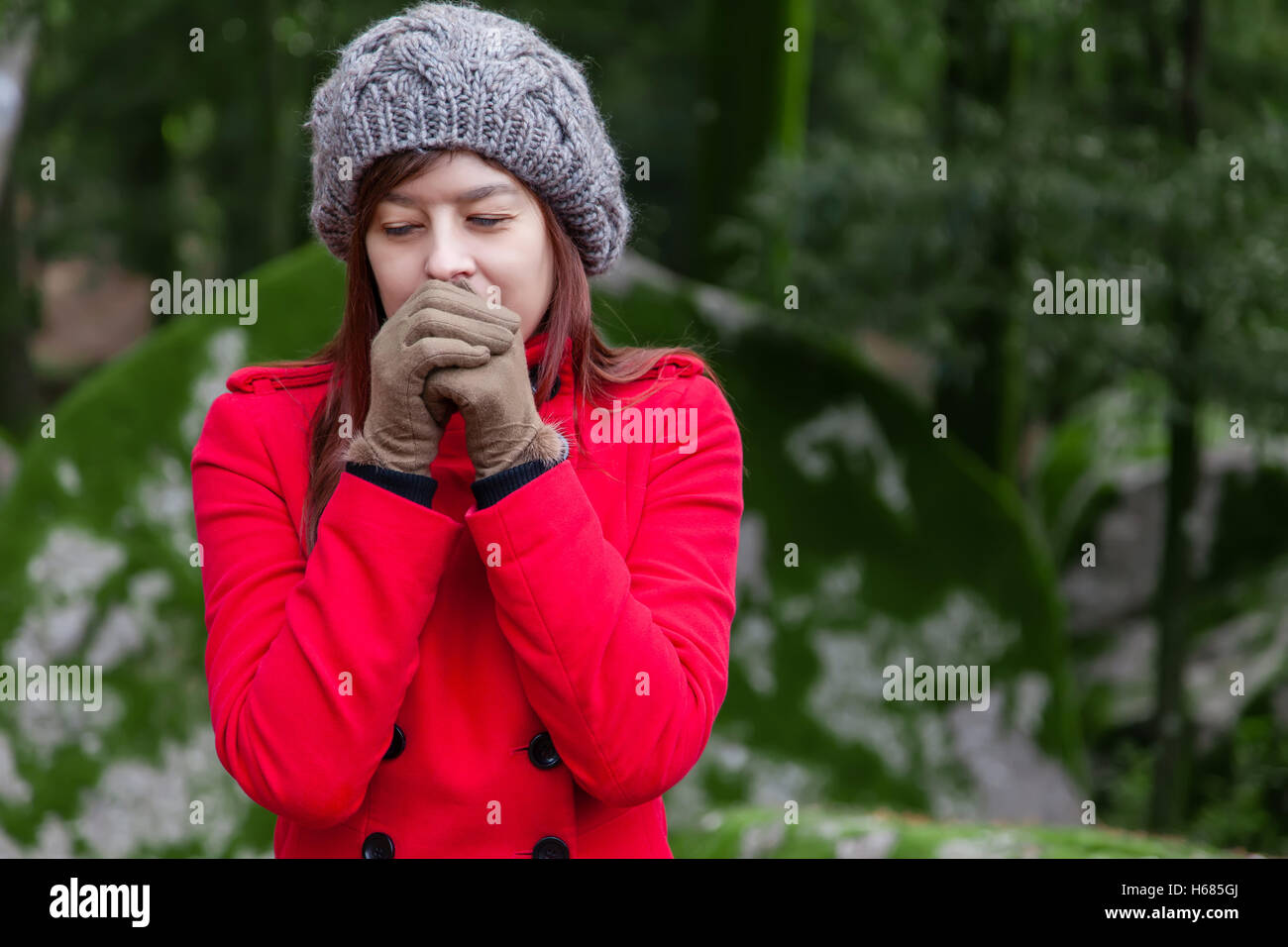 Frau, die vor Kälte zitternd und bläst warme Luft an den Händen auf einen Wald tragen einen roten Mantel, eine Mütze und Handschuhe im winter Stockfoto