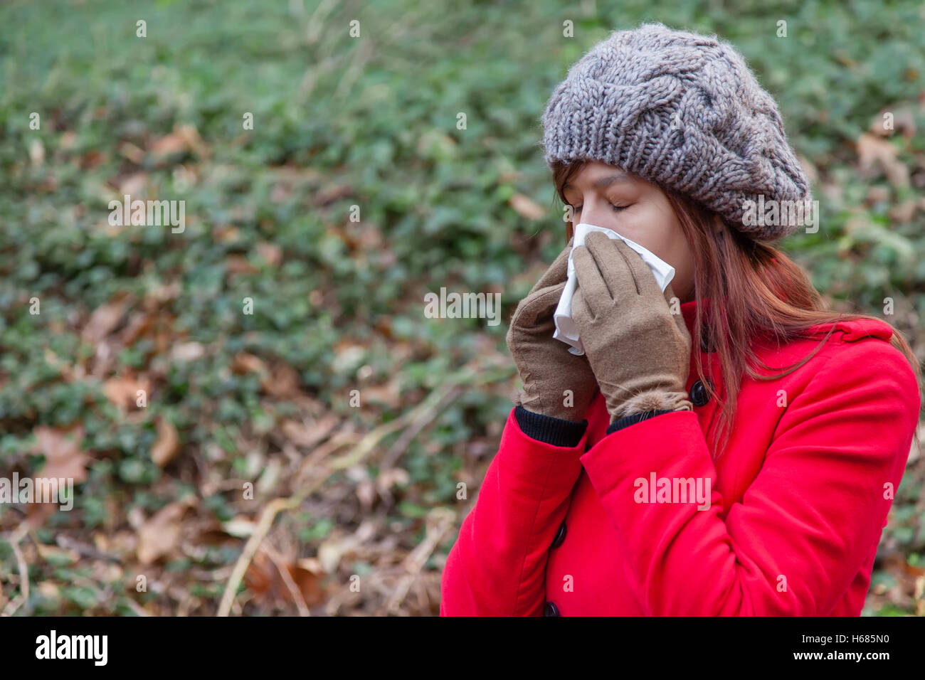 Frau mit einer Erkältung oder Grippe Niesen zu einem Papiertaschentuch auf einen Wald tragen einen roten Mantel, eine Mütze und Handschuhe im winter Stockfoto