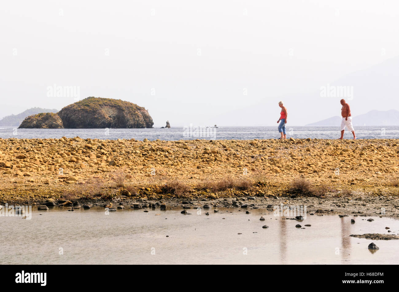 Zwei Menschen gehn an einem steinigen Strand auf einer türkischen Insel Stockfoto