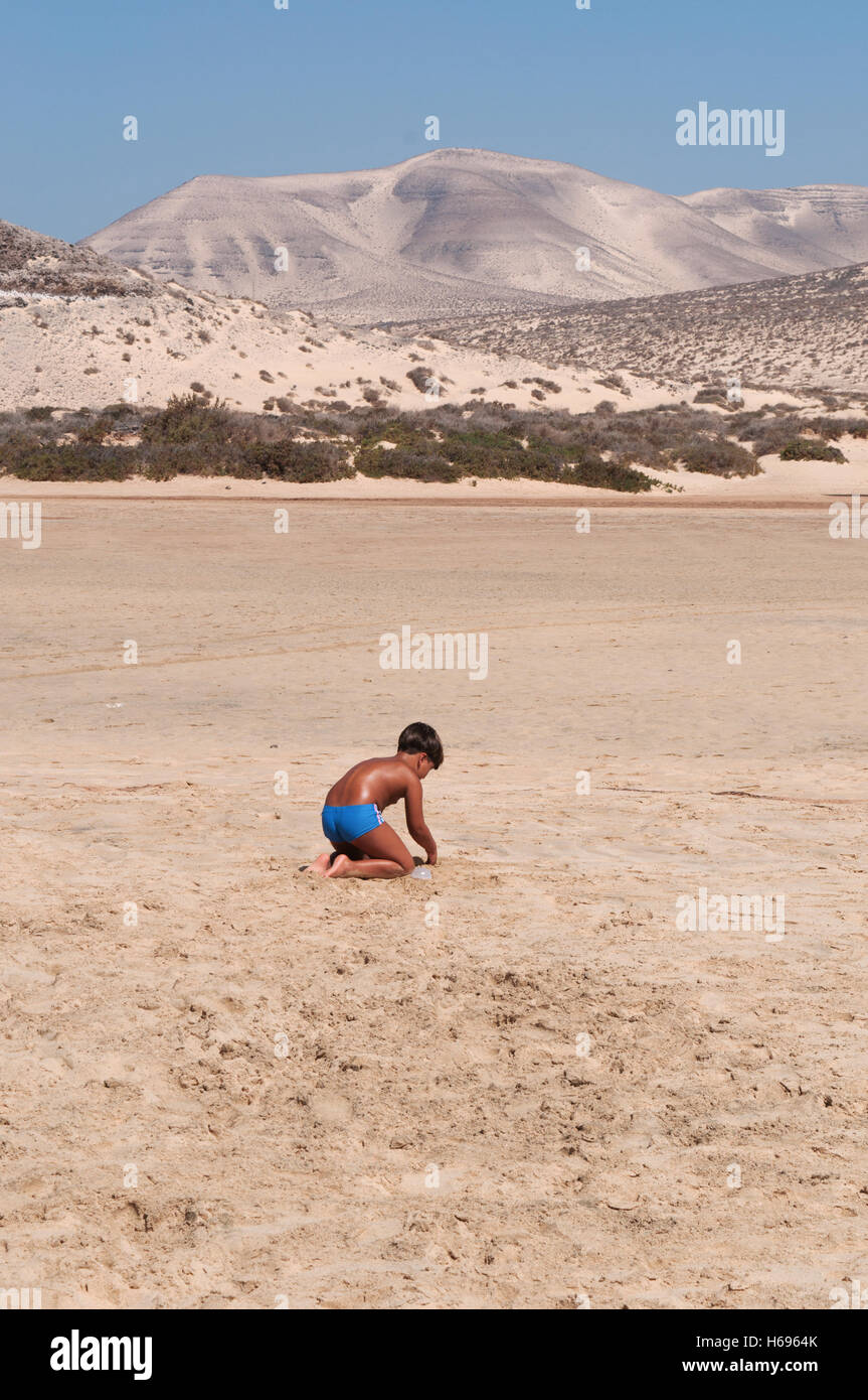 Fuerteventura, Kanarische Inseln, Nordafrika, Spanien: ein Kind beim Spielen im Sand in der Wüste Landschaft der Strand von Playa de Jandia Stockfoto