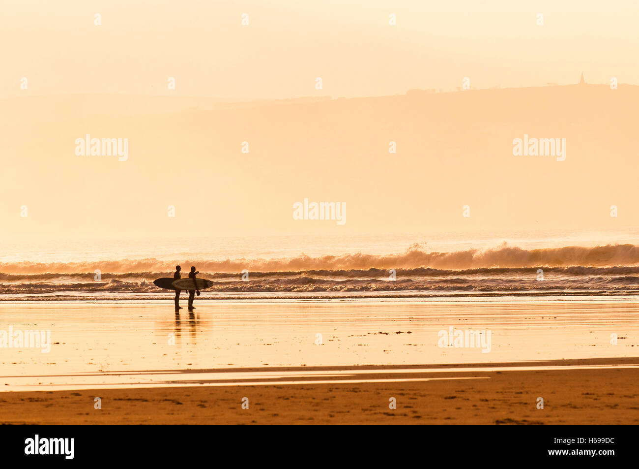 Am frühen Morgensonnenlicht erfüllten zwei Surfer auf Gwithian Towans Strand in Cornwall. Stockfoto