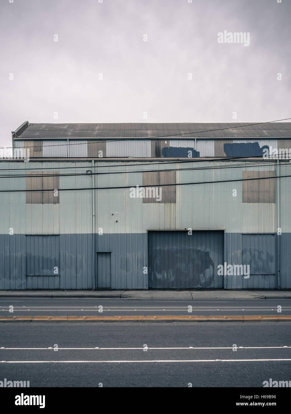 Altes Lagerhaus bemalt blau und grau mit gereinigten Graffiti und überdachte und schöne Türen an einem flachen, bewölkten Tag Stockfoto