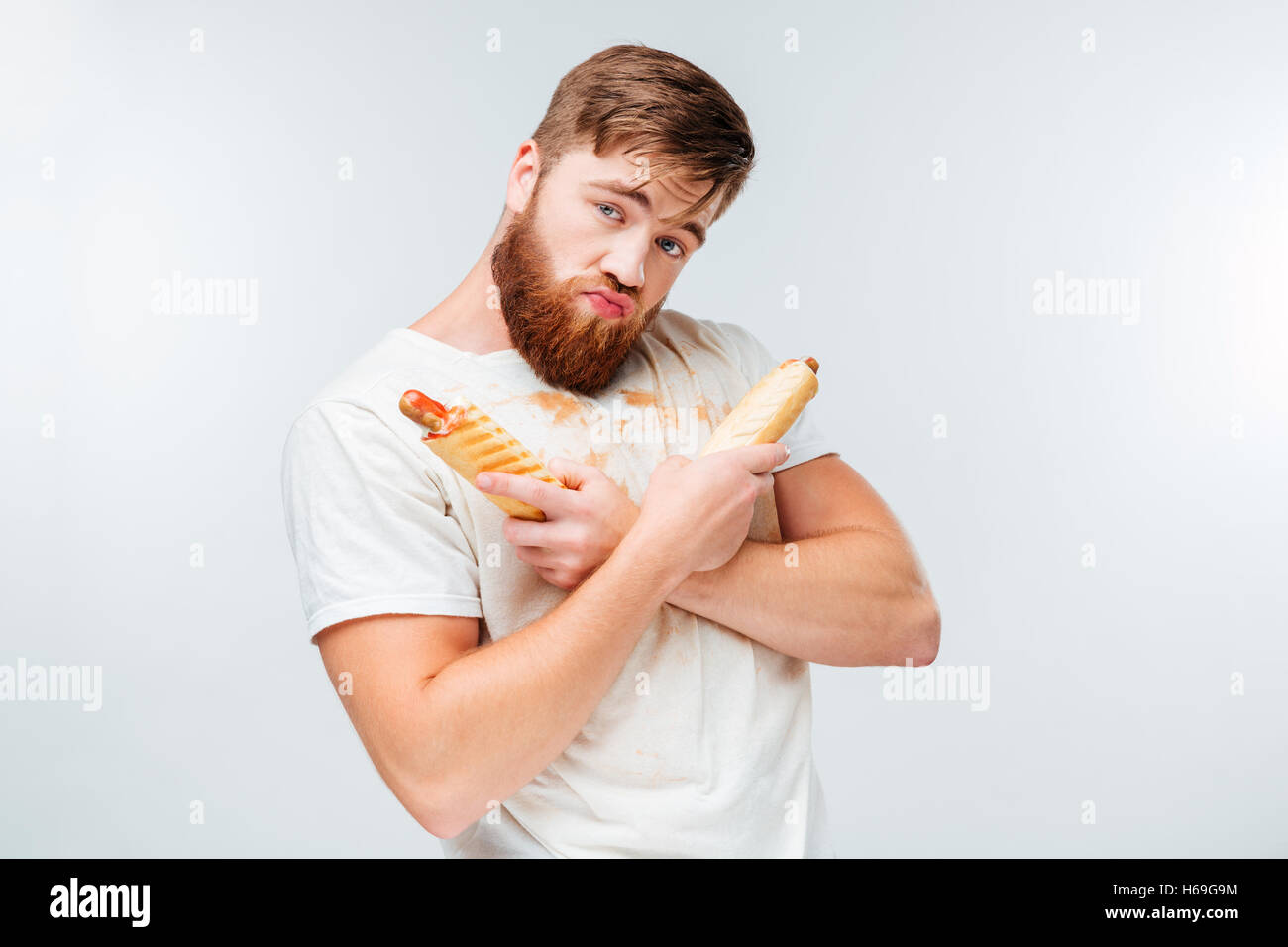Young bärtiger Mann in dreckigen Shirt hält zwei Hotdogs isoliert auf weißem Hintergrund Stockfoto