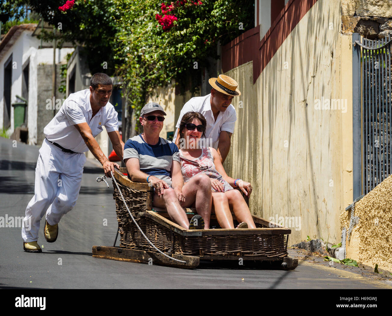 Rodel-Fahrer, gekleidet in traditioneller weißer Kleidung tragen Touristen in hölzernen Schlitten vom Monte den Hügel hinunter nach Funchal Stockfoto