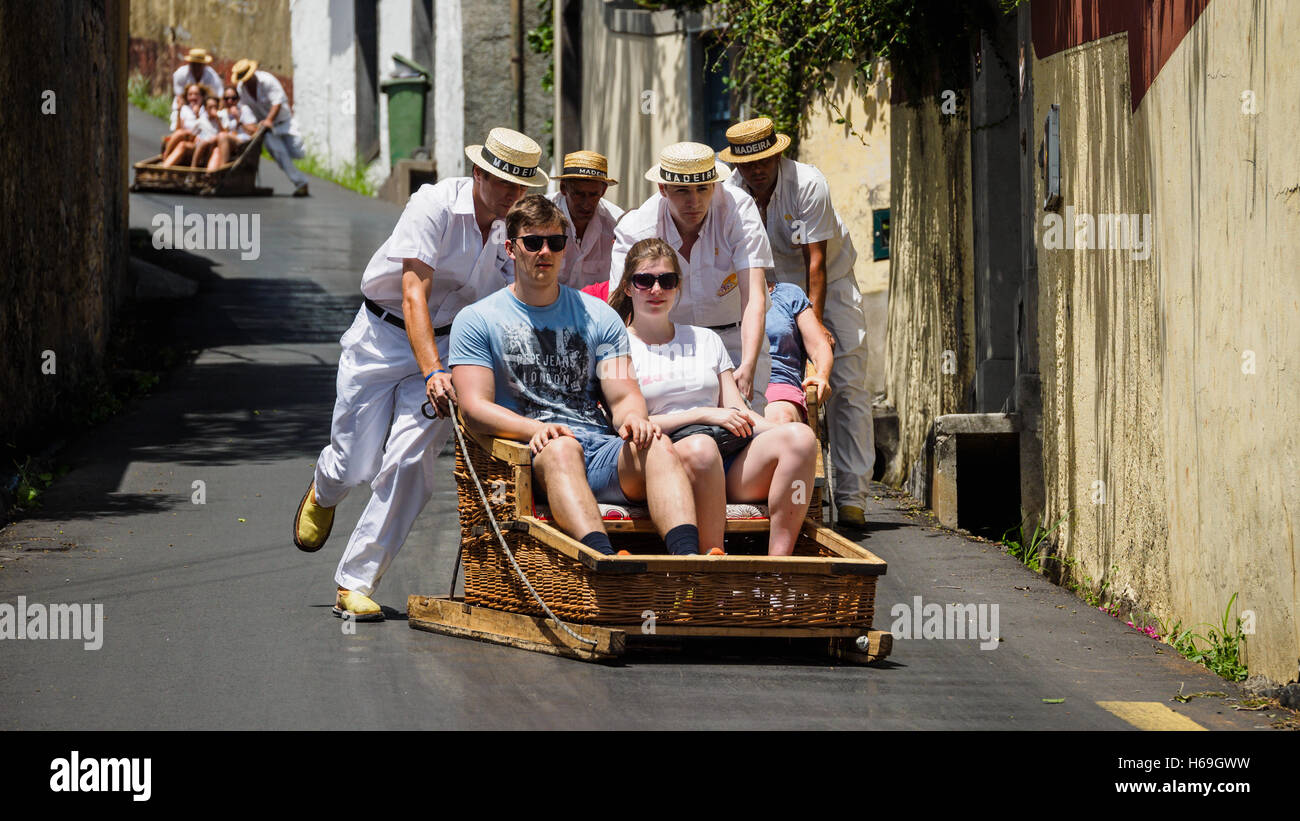 Rodel-Fahrer, gekleidet in traditioneller weißer Kleidung tragen Touristen in hölzernen Schlitten vom Monte den Hügel hinunter nach Funchal Stockfoto