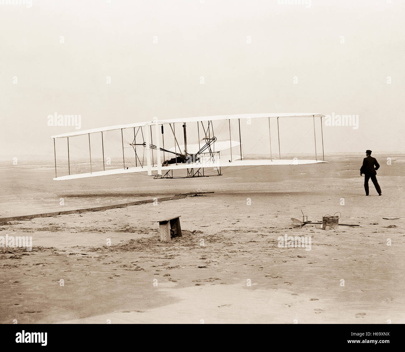 Ersten Flug der Gebrüder Wright. 120 Fuß in 12 Sekunden; Kitty Hawk, North Carolina.The Foto zeigt Orville Wright am Steuer die Flugmaschine Bauchlage auf der unteren Tragfläche mit Hüften in die Wiege, die den Flügel-verwerfen Mechanismus betrieben. Wilbur Wright läuft neben die Maschine auszugleichen hat soeben seinen Einfluss auf die vorwärts aufrechte des rechten Flügels. Der Start Schiene, Flügel-Rest, eine Spule-Box und andere Gegenstände benötigt zur Flugvorbereitung sind sichtbar hinter der Maschine. Foto von John T. Daniels Stockfoto Ersten Flug der Gebrüder Wright. 120 Fuß in 12 Sekunden; Kitty Hawk, North Carolina.The Foto zeigt Orville Wright am Steuer die Flugmaschine Bauchlage auf der unteren Tragfläche mit Hüften in die Wiege, die den Flügel-verwerfen Mechanismus betrieben. Wilbur Wright läuft neben die Maschine auszugleichen hat soeben seinen Einfluss auf die vorwärts aufrechte des rechten Flügels. Der Start Schiene, Flügel-Rest, eine Spule-Box und andere Gegenstände benötigt zur Flugvorbereitung sind sichtbar hinter der Maschine. Foto von John T. Daniels Stockfoto