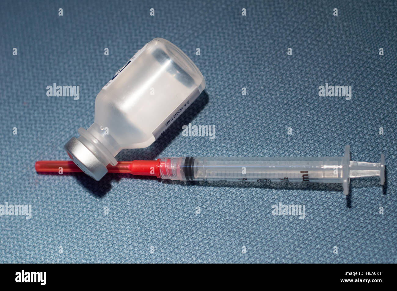 Leere Spritze mit Nadel und Fläschchen von Medikamenten auf blauem Tuch Hintergrund Stockfoto