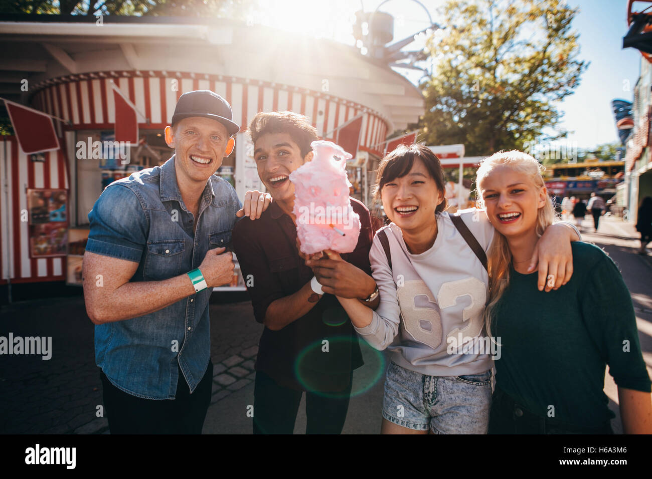 Gruppe von glücklichen jungen Freunden mit Zuckerwatte im Vergnügungspark. Junge Männer und Frauen halten Baumwolle Zuckerwatte und lächelnd. Stockfoto