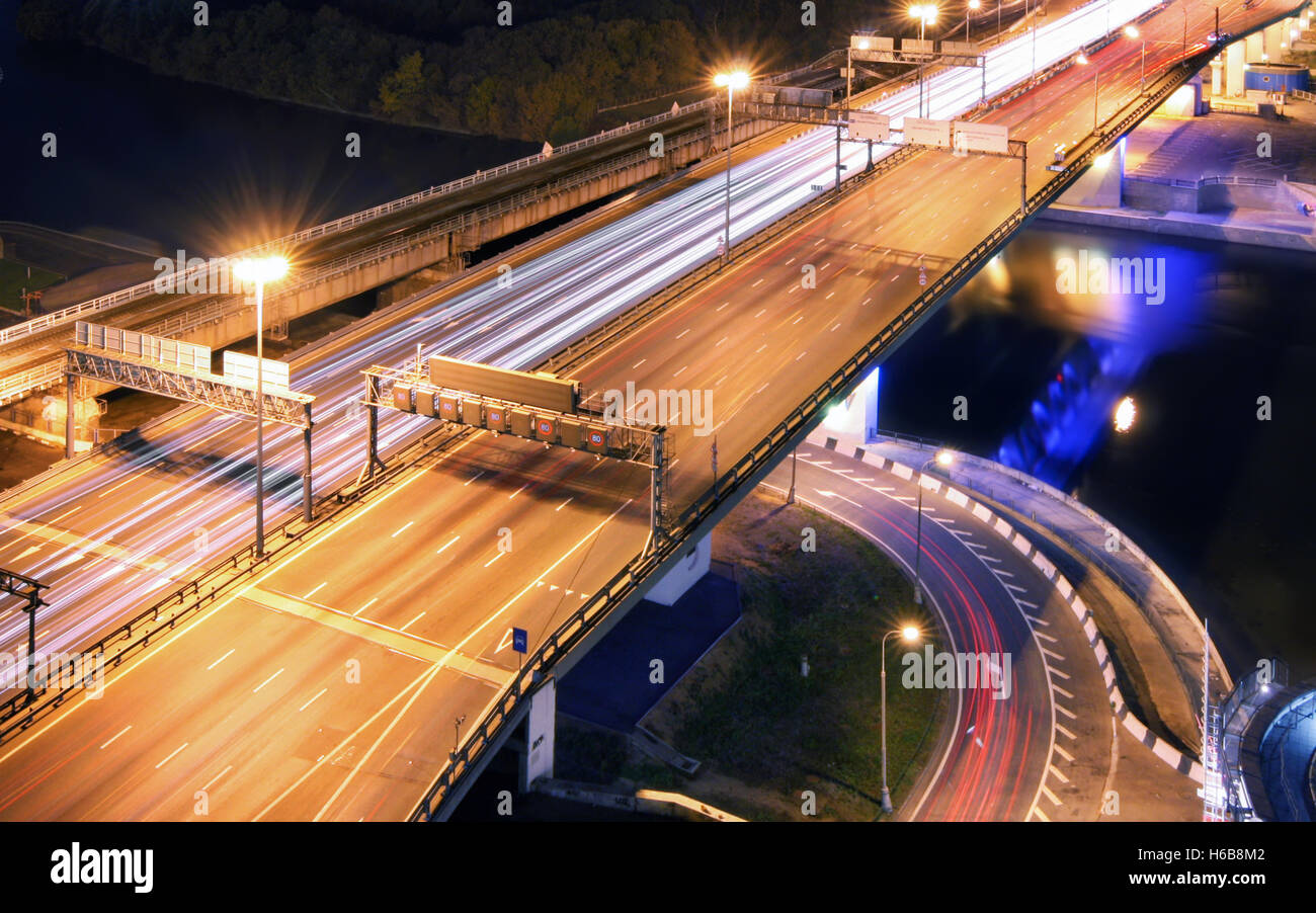 Straßenbrücke über den Fluss in der Nacht, Ansicht von oben. Lichtspuren des Autos auf einer Autobahn Stockfoto