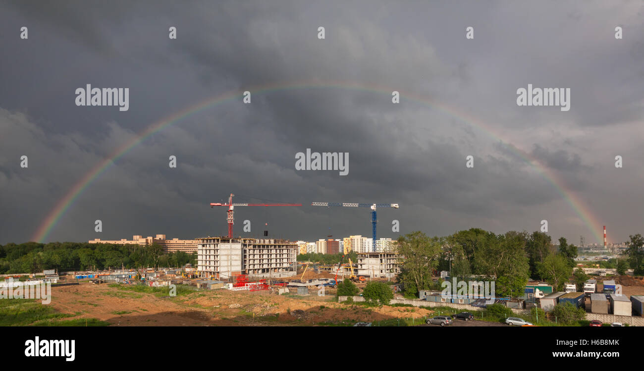 Stürmischer Himmel mit einem vollen Regenbogen über der Baustelle eines Wohnhauses mit Turmdrehkranen Stockfoto