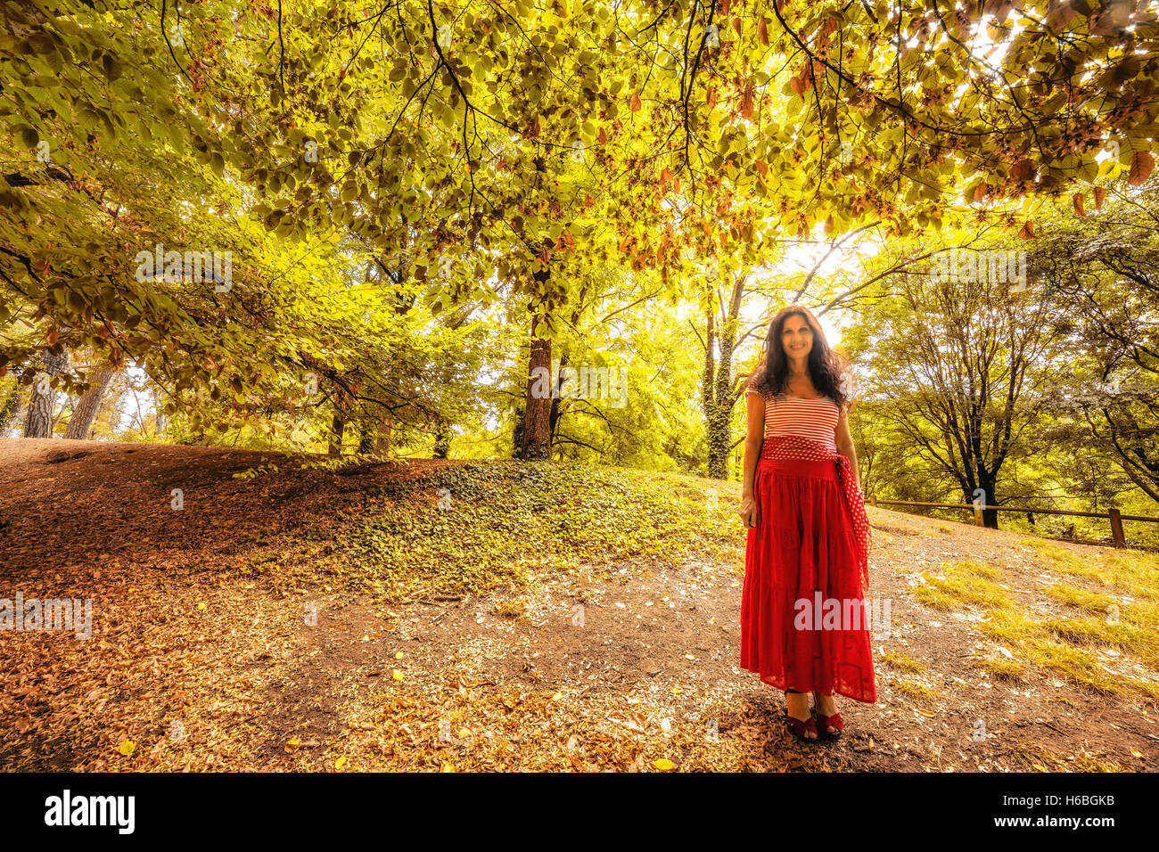 Reife Frau gekleidet in Zigeuner Kleid mit roten Rock und T-shirt aus Baumwolle mit Bateau-Ausschnitt im öffentlichen Park mit Boden fallenden Laub Stockfoto