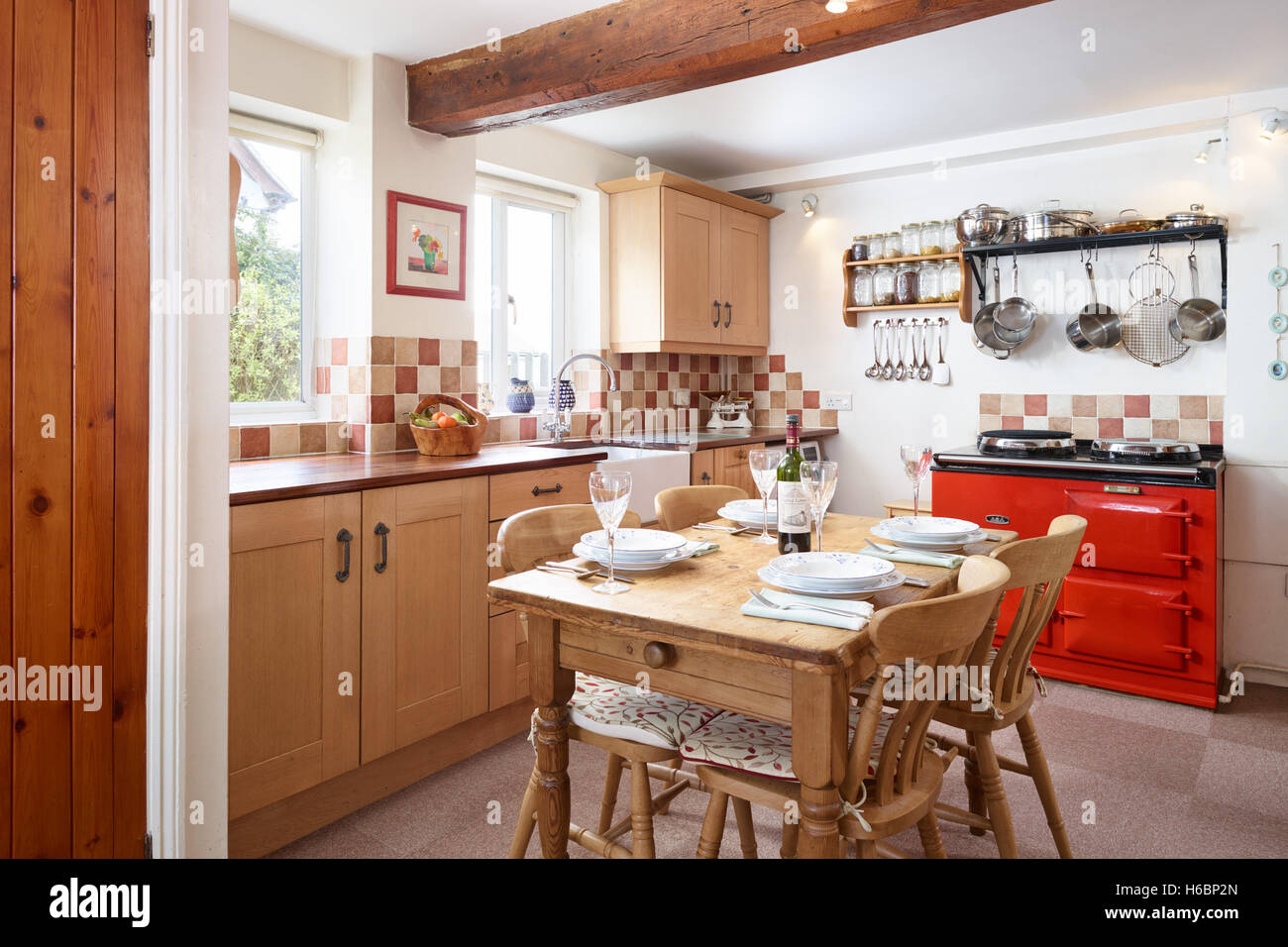 Eine traditionelle, frische Landhausküche zeigt eine rote Aga, Tabelle, Einheiten & Arbeitsflächen. Gloucestershire, UK Stockfoto