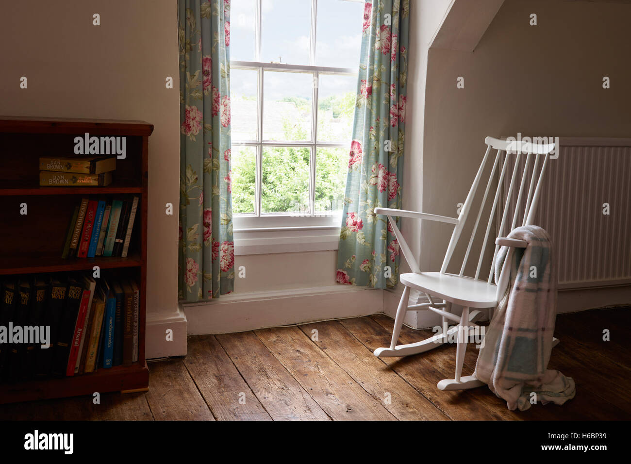 Einem weißen, leeren Schaukelstuhl auf ein Massivholzboden durch ein Fenster in einem Raum mit einem Wurf über den Arm. Stockfoto
