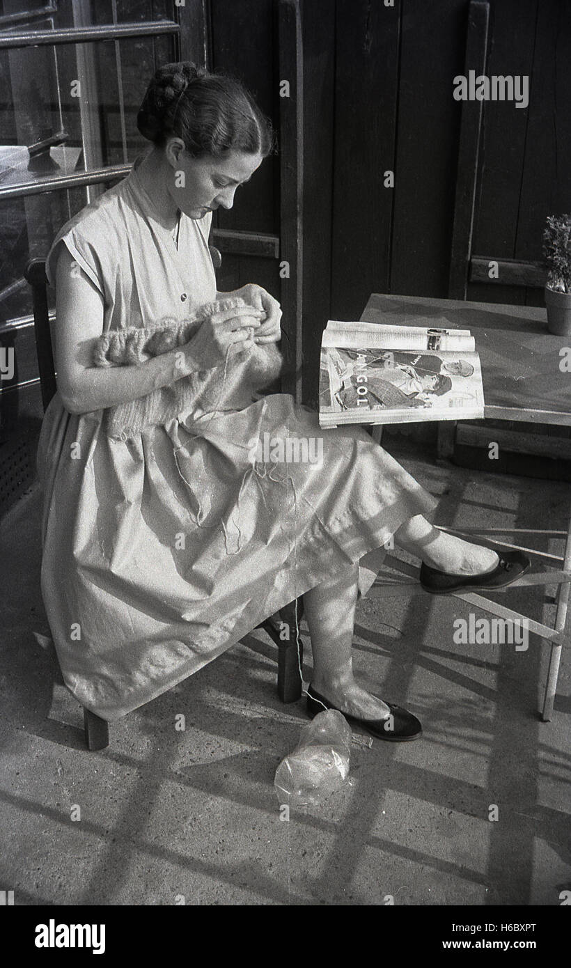 1940er Jahre, historische, junge Dame stricken auf Garten Veranda, England, UK. Sie liest eine Zeitschrift mit einer Werbeanzeige für britische Bekleidungsunternehmen Kangol. Stockfoto