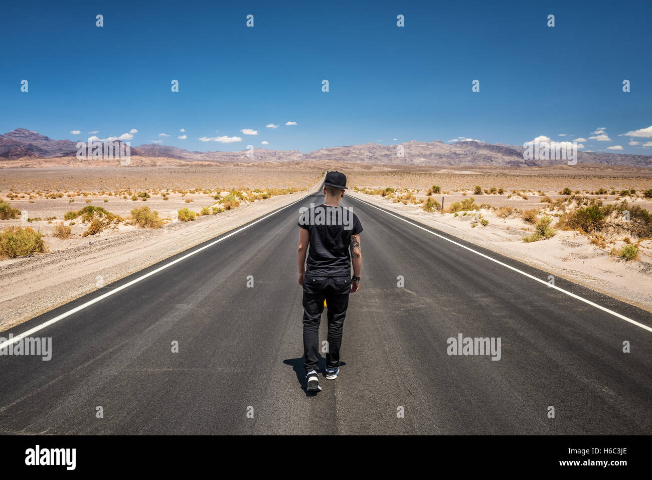 Junger Mann allein durch eine leere Straße in der Wüste des Death Valley National Park an einem sonnigen Tag zu Fuß Stockfoto