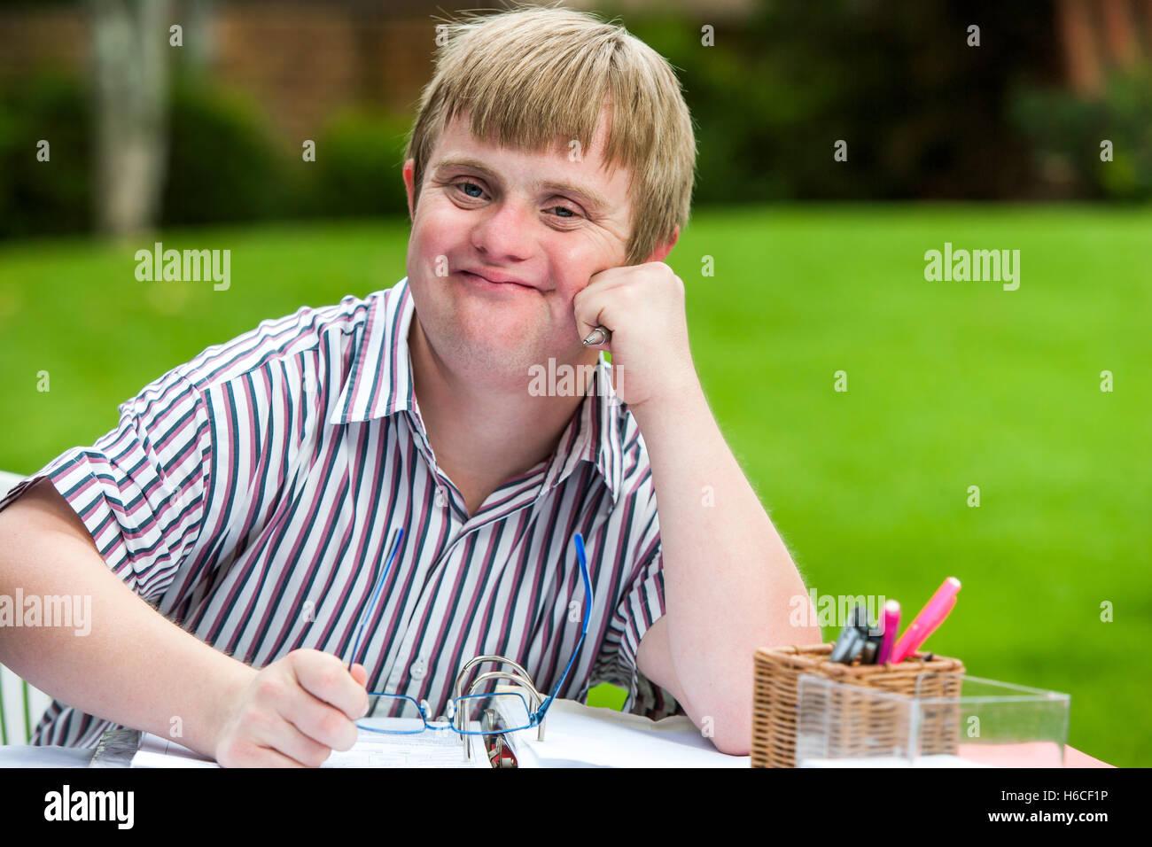 Porträt des jungen Männern Schüler mit Down-Syndrom am Schreibtisch hält Gläser hautnah. Stockfoto