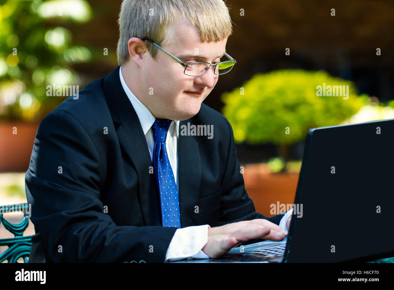 Porträt der Geschäftsmann mit Down-Syndrom arbeiten hautnah. Junger Mann im Anzug auf Laptop im Garten arbeiten. Stockfoto