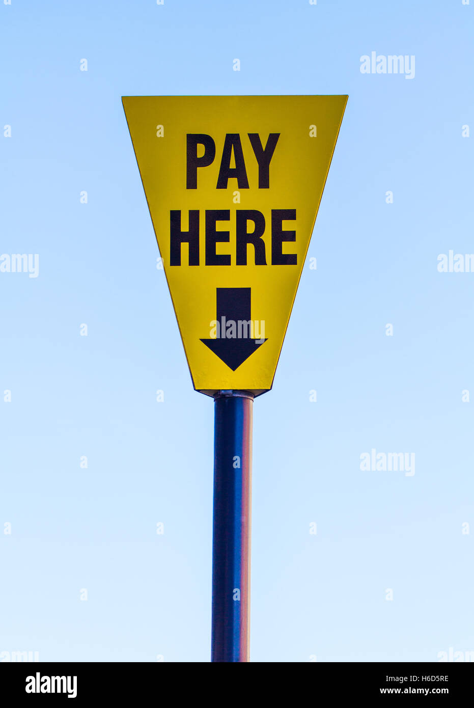Ein helles gelbes Schild mit den Worten zahlen hier auf und einem Pfeil, der nach unten mit einem blauen Himmel im Hintergrund. Stockfoto
