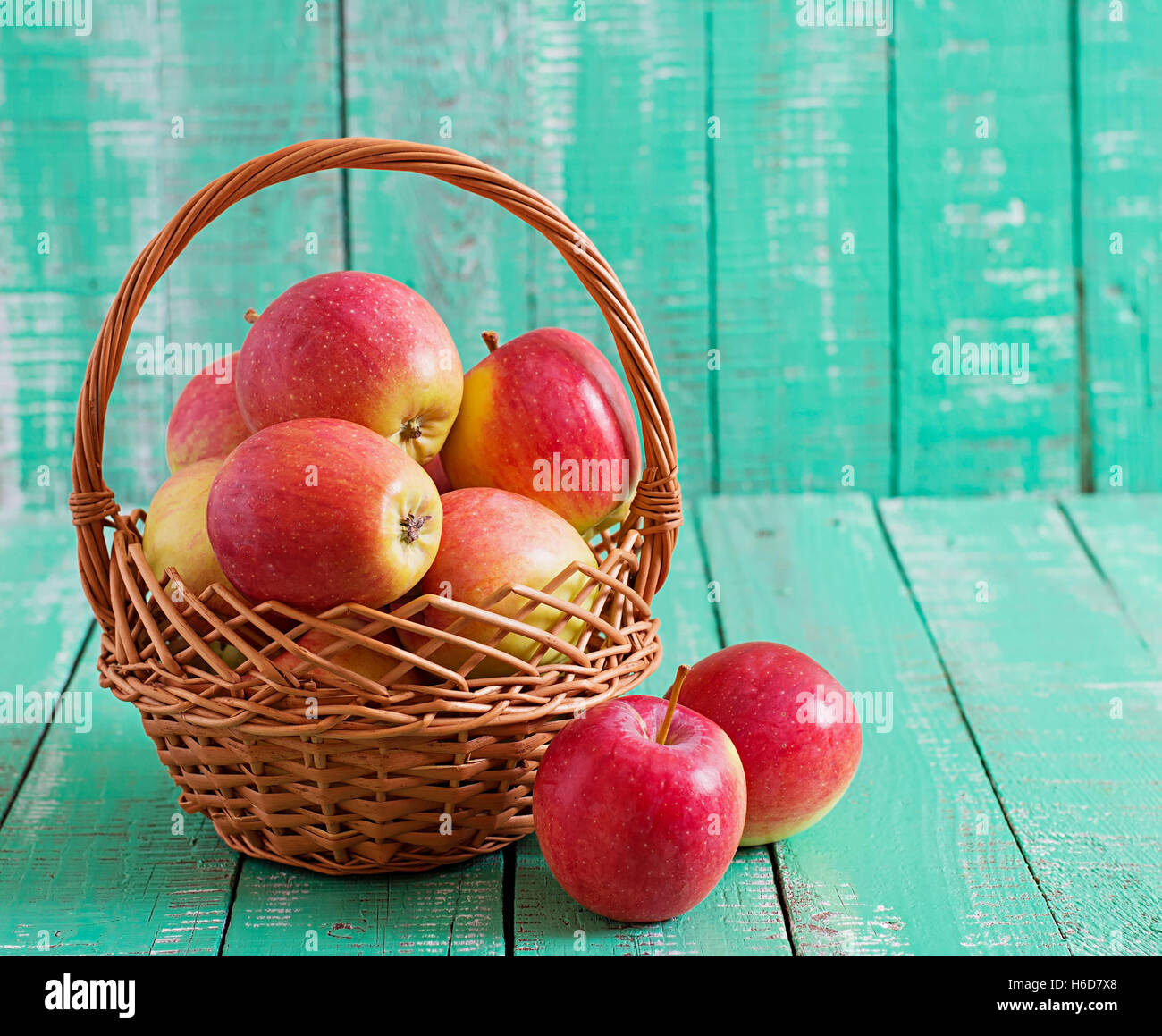 Reife rote Äpfel in einem Korb auf einem hellen Hintergrund aus Holz. Stockfoto