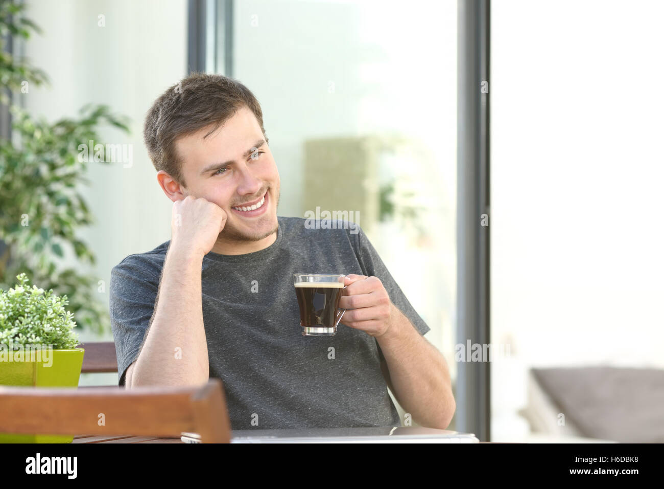 Gut aussehender Mann, entspannend, trinken Kaffee sitzen in einer Tabelle in einen Balkon von einem Hotelzimmer oder zu Hause Stockfoto