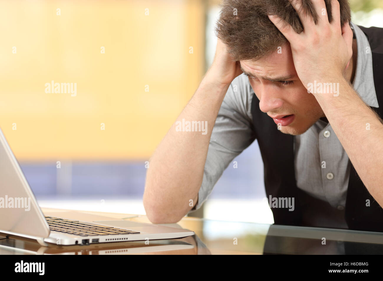 Nahaufnahme eines besorgt Unternehmers gerade Laptop mit den Händen auf dem Kopf sitzen in einem Schreibtisch in einem Büro indoor Stockfoto