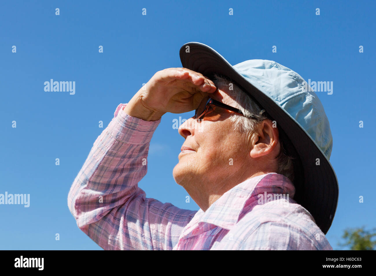 Eine ältere Frau mit einem breiten Sonnenhut und Sonnenbrille im Sonnenschein Krempe Schattierungen ihre Augen weit bis in die Sonne zu schauen im Sommer. England Großbritannien Großbritannien Stockfoto