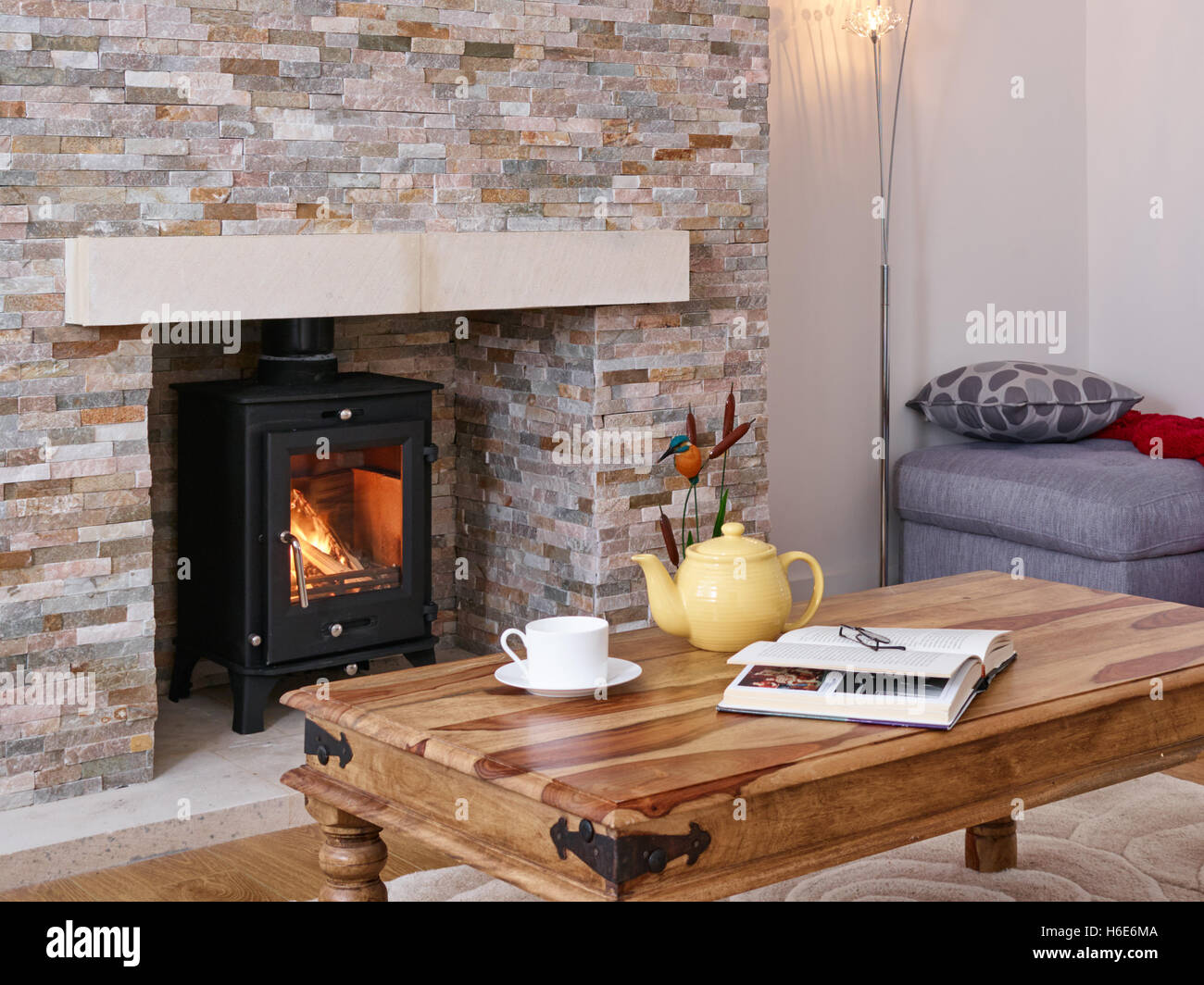 Ein Couchtisch mit einem Buch, einer Teekanne & Teetasse in ein gemütliches Wohnzimmer mit Holzverbrennung Herd. UK Stockfoto