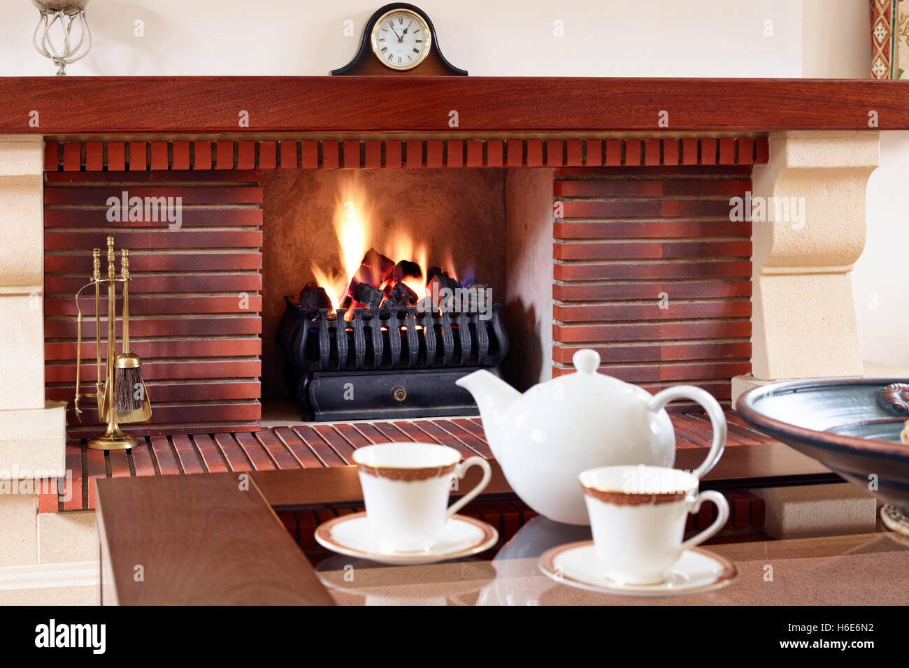 Ein Tisch mit einer Teekanne und Teetassen in einem komfortablen Wohnzimmer mit Kamin.de Stockfoto