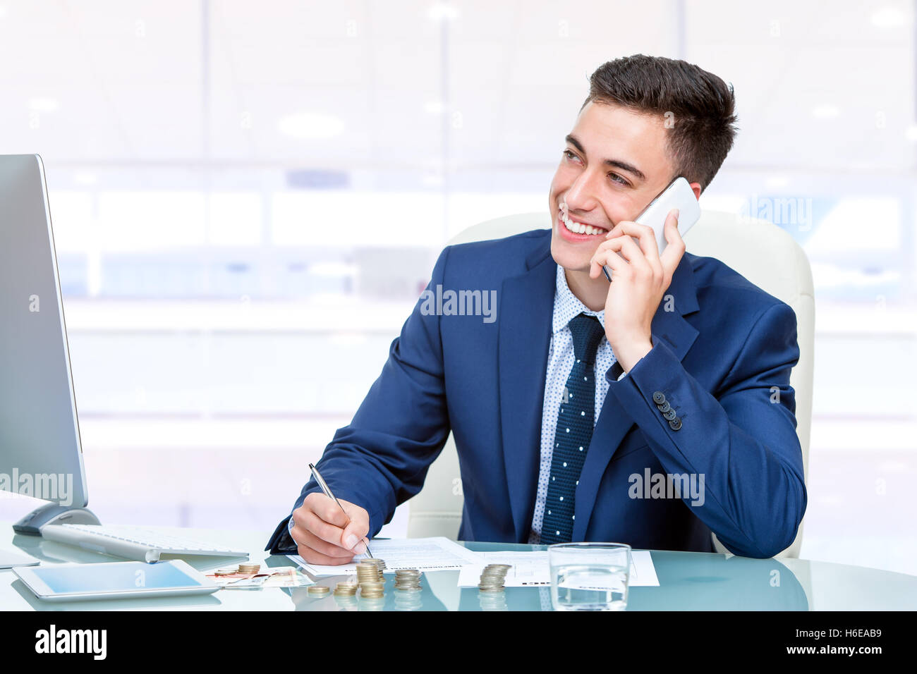 Porträt von attraktiven jungen Buchhalter am Smartphone im Büro sprechen hautnah. Junger Mann am Schreibtisch vor dem Computer. Stockfoto