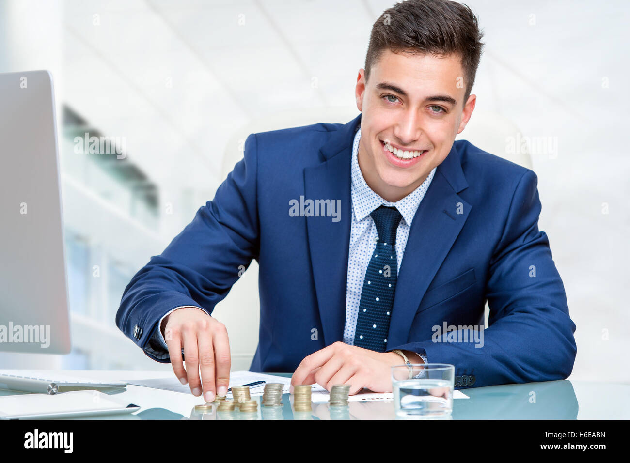Porträt des jungen Buchhalters Geldzählen am Schreibtisch hautnah. Jungunternehmer im blauen Anzug sitzt am Schreibtisch im Büro. Stockfoto