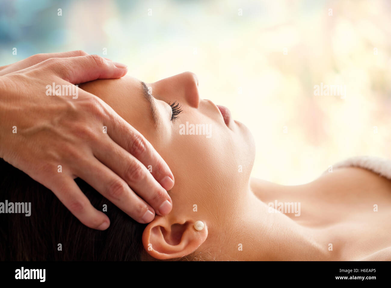 Kopf-Porträt der jungen Frau, die Gesichts-Massage im Spa hautnah. Therapeuten massieren Frauenkopf vor bunten Hintergrund Stockfoto