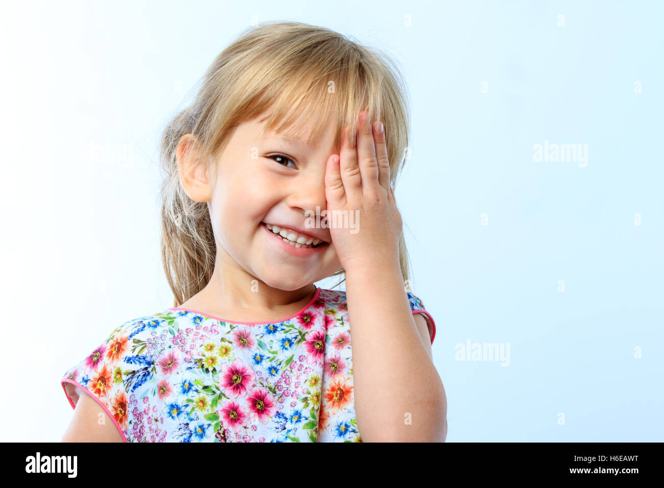 Porträt der niedliche kleine Mädchen schließen ein Auge mit der Hand vor blauem Hintergrund hautnah. Stockfoto