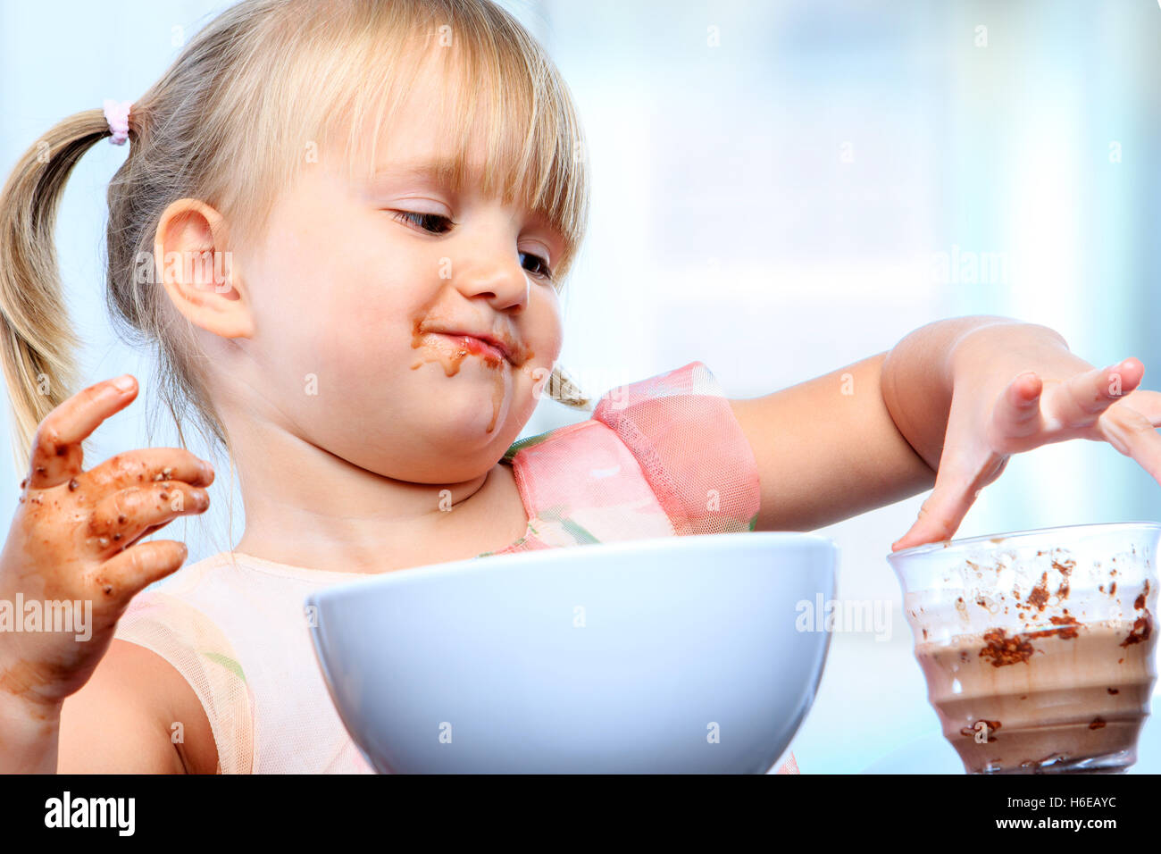 Porträt von kleinen Mädchen beim Frühstück hautnah. Säugling verschütten und Herumspielen mit Schokomilch. Stockfoto