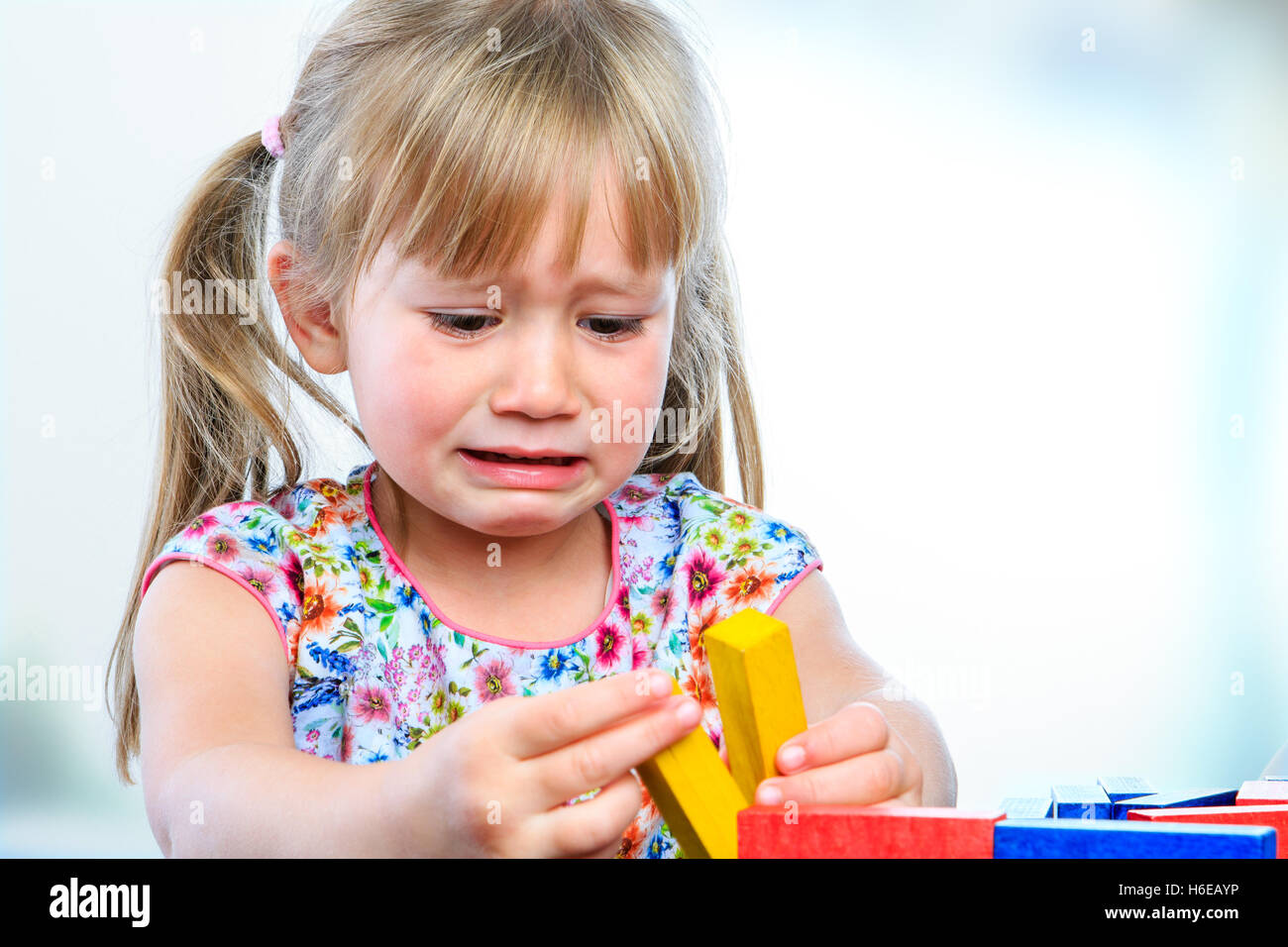 Porträt von weinenden Mädchen spielen mit Holzklötzen am Tisch hautnah. Frustriert Girl zeigt launisch Verhalten und langes Gesicht Stockfoto